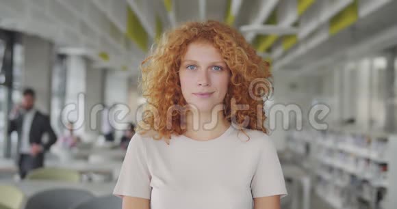 站在现代办公工作区的卷曲红头发经理的正面视图迷人的微笑年轻女子的肖像视频的预览图