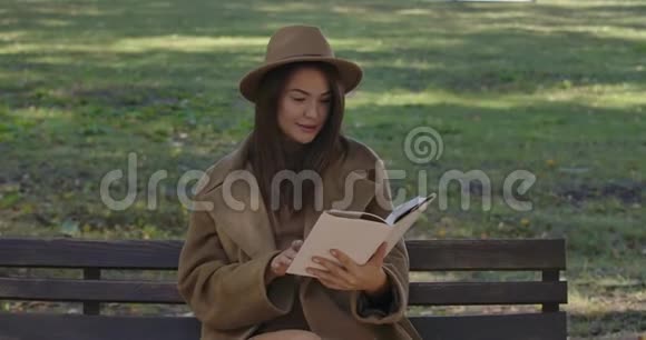 可爱的高加索女学生穿着优雅的棕色衣服坐在长凳上翻书页聪明的人视频的预览图