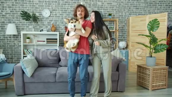 一对幸福的夫妇抱着威尔士科吉彭布罗克狗在家里跳舞视频的预览图