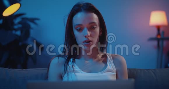 一个悲伤的年轻女子在看电影中的一个感人的场景时忧心忡忡心烦意乱的女孩膝盖上拿着笔记本看着视频的预览图