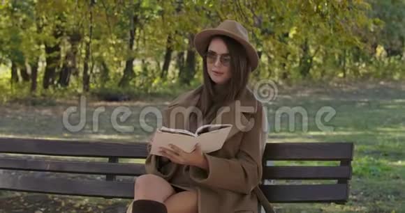 聪明优雅的高加索女人戴着太阳镜和棕色帽子坐在长凳上翻书页美丽美丽视频的预览图