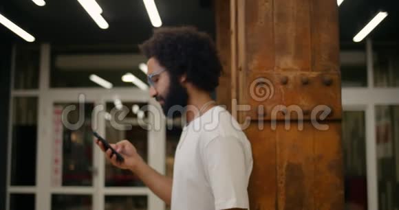 站在30多岁的家伙靠在一边用他的智能手机戴眼镜的帅哥看手机屏幕视频的预览图
