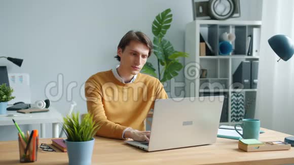 精疲力竭的家伙用笔记本电脑打字然后摸着头在工作中感到疲倦视频的预览图