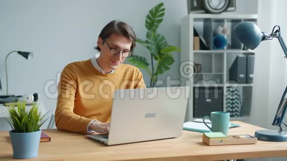 开朗的家伙用笔记本电脑打字在办公室的桌子上专心工作视频的预览图