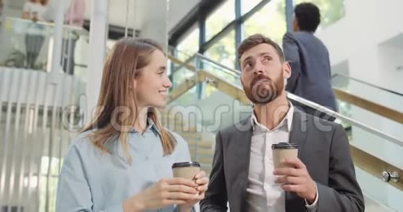 男女员工休息时拿着纸杯站在办公室大厅交谈帅哥男工视频的预览图
