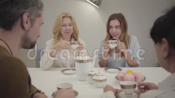 不同年龄的亲戚或朋友坐在桌子旁喝茶喝咖啡说话的肖像快乐的人视频的预览图