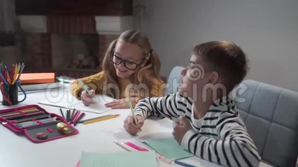 两个快乐的白人孩子在练习本上写字和说话的画像戴眼镜的女孩和坐在旁边的男孩视频的预览图