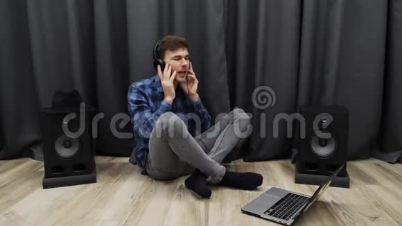 戴着耳机听音乐唱歌的人年轻的音乐家坐在地板上用笔记本在耳机里唱歌视频的预览图