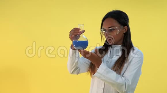 戴着安全眼镜和实验室外套的漂亮黑人女人手里拿着液体的瓶子视频的预览图