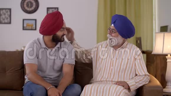 坐在沙发上的印度父子在家里开怀大笑幸福的家庭在一起视频的预览图