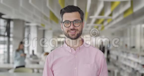 戴眼镜的快乐商人站在办公室现代室的肖像微笑的首席执行官的正面视角视频的预览图