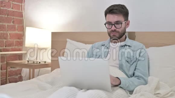 雄心勃勃的男性设计师在床上庆祝笔记本电脑的成功视频的预览图