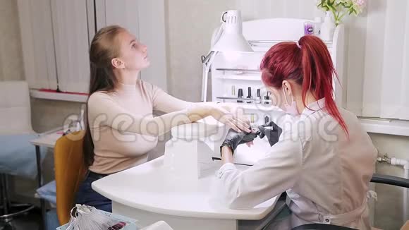 一家美容院带手套的女美甲师在涂胶前客户的指甲去掉视频的预览图
