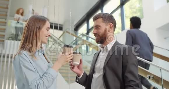 两位不同的办公室同事从纸杯里喝咖啡并进行交谈男性和女性同事交谈视频的预览图