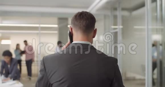 男性商人在智能手机上交谈和进入现代办公室的背面视图男女办公室工作人员视频的预览图