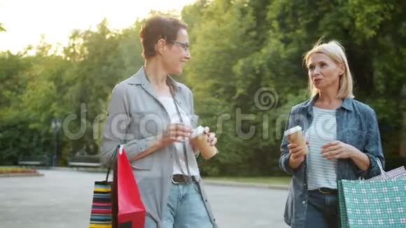 美女拿着购物袋和咖啡在外面聊天的慢动作视频的预览图