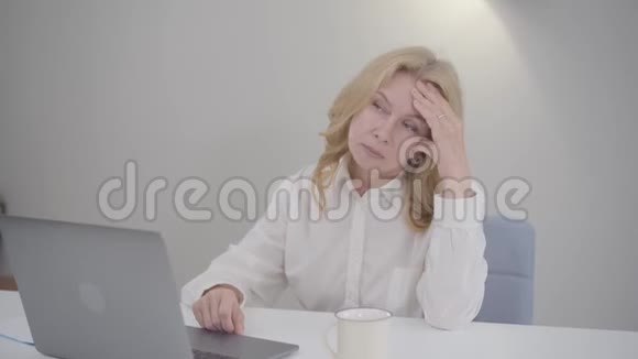 一位忧心忡忡的高加索老太太拿着笔记本电脑坐在桌旁在家工作的成熟商务女士视频的预览图