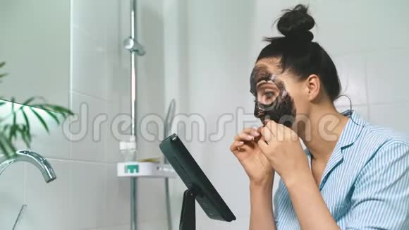 一个年轻漂亮的黑发女人用面具在浴室里洗脸视频的预览图