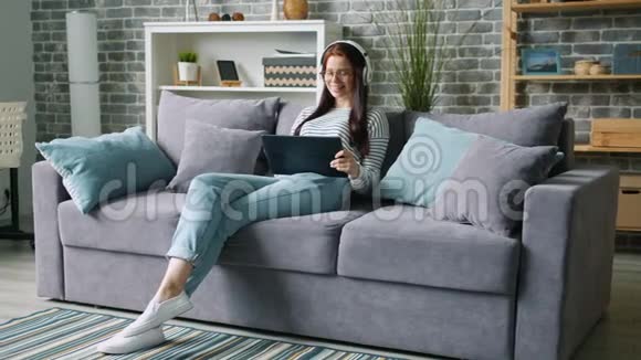 美女戴着耳机坐在沙发上用平板电脑放松视频的预览图