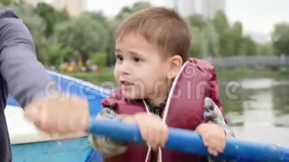 在湖边的公园里努力划船的小有趣的孩子湖面上情绪激动的小男孩的画像可爱的孩子坐在船上视频的预览图