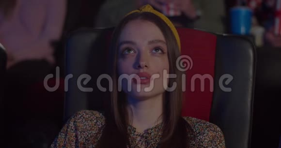 千禧一代女性坐在椅子上对电影中令人兴奋的时刻产生敬畏的反应美女在看视频的预览图