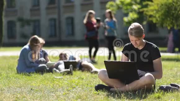 帅哥男生在公园里用笔记本电脑学习视频的预览图
