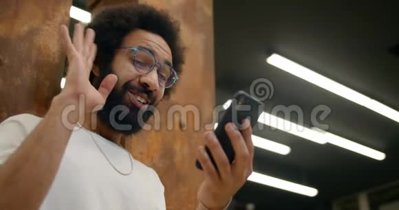 在智能手机上进行视频对话时30多岁兴奋的家伙微笑和挥手的底部视图戴眼镜的男人视频的预览图