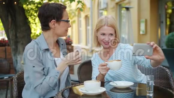 快乐的朋友在咖啡馆里自拍用智能手机装饰头发和花视频的预览图