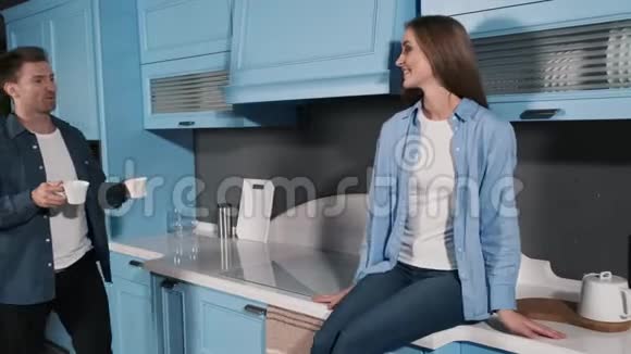 快乐夫妇在厨房里喝早咖啡站在厨房里聊天喝咖啡的年轻男女视频的预览图