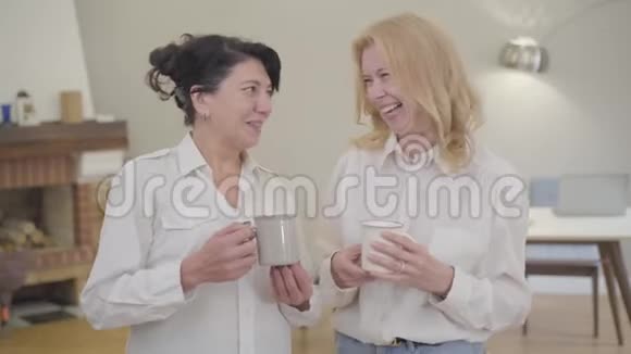 两个白人妇女站在房间里喝着茶或咖啡说话成熟的朋友或姐妹视频的预览图