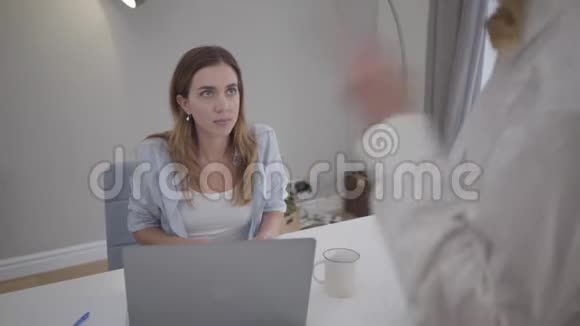 不认识的女人骂年轻漂亮的白人女孩坐在桌子上拿着笔记本电脑新女性雇员视频的预览图