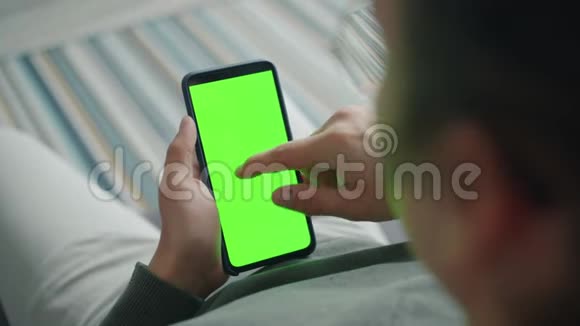 一个人独自坐在家里一个人拿着绿色屏幕色度键智能手机视频的预览图