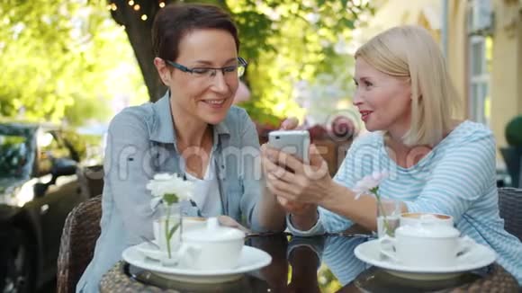 在城市大街的露天咖啡馆里使用智能手机的兴奋女性大笑视频的预览图