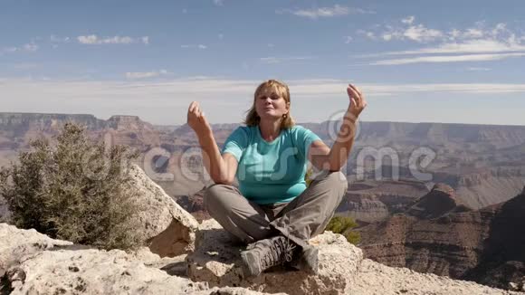 成年女性徒步旅行者坐在大峡谷国家公园顶上冥想视频的预览图
