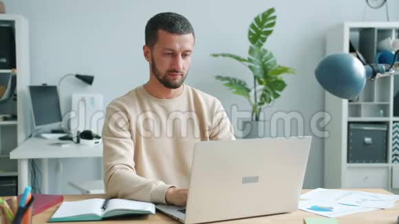 精疲力竭的黑发男子在室内工作时使用电脑触摸面部和头部视频的预览图