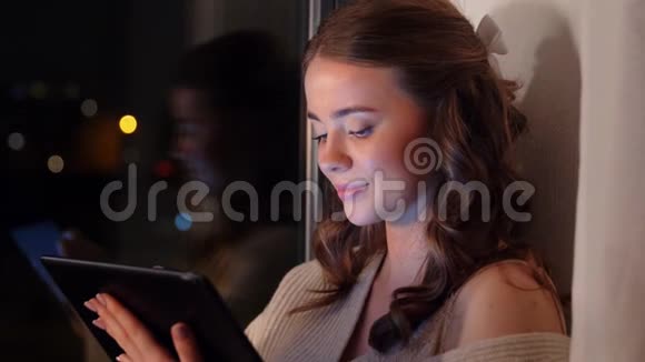 坐在窗前拿着平板电脑的年轻女子视频的预览图