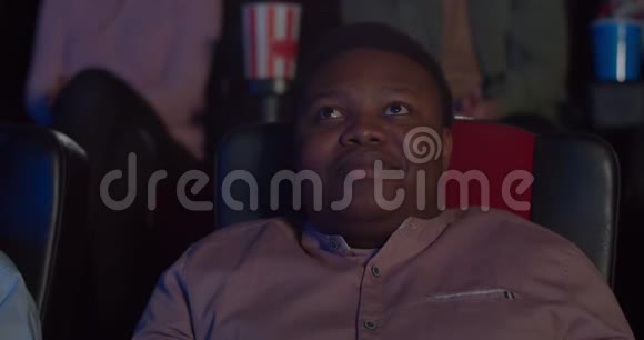 在电影院里幸福的年轻人脸上贴着喜剧片千禧一代非洲男人坐在椅子上笑着视频的预览图