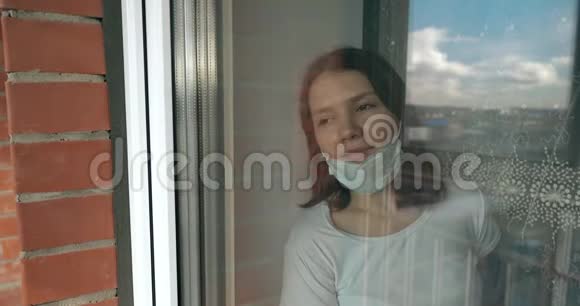 一个戴着医用口罩的年轻女孩从窗口望向街上他公寓里女孩的自我隔离视频的预览图