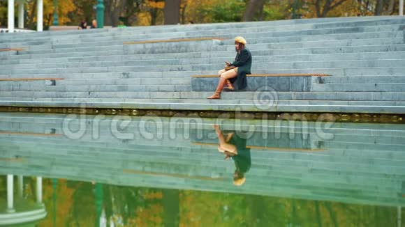 寂寞女孩坐在靠近池塘的楼梯上发短信视频的预览图