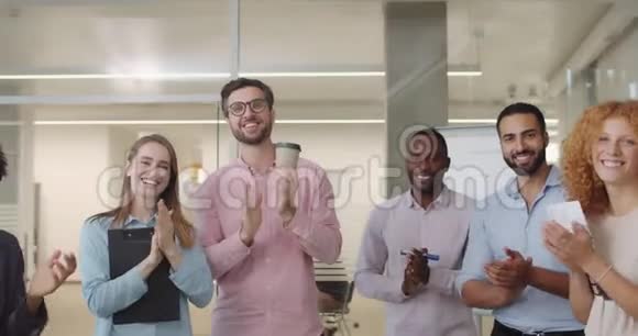 一群笑容可掬的幸福的多种多样的工人在办公室里鼓掌站着多民族男女视频的预览图