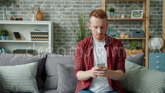一个快乐的男人在家里用智能手机触摸屏幕独自笑着休息视频的预览图