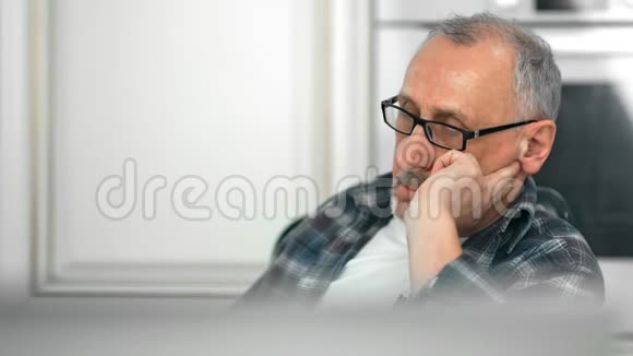 一个戴着眼镜闭着眼睛在白色房间里打盹的疲惫的成熟白发男子视频的预览图