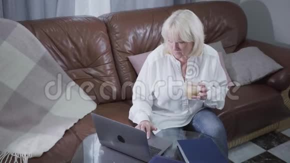 一位迷人的高加索人女性在笔记本电脑屏幕上观看照片和微笑的俯视图金发成熟视频的预览图