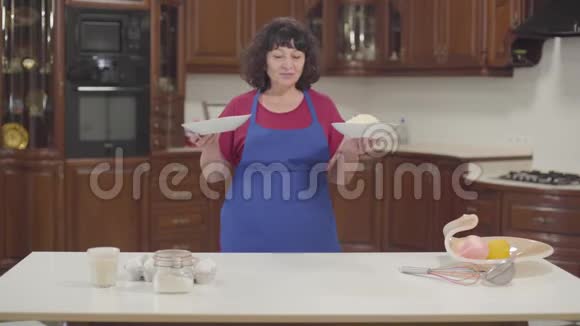 成熟的白种人黑发女人把两个盘子放在桌子上一个盘子是空的另一个装满面粉视频的预览图