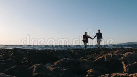 年轻人牵着女朋友手在日落在海滩上散步男人和女人在海滩上享受大海爱的剪影视频的预览图