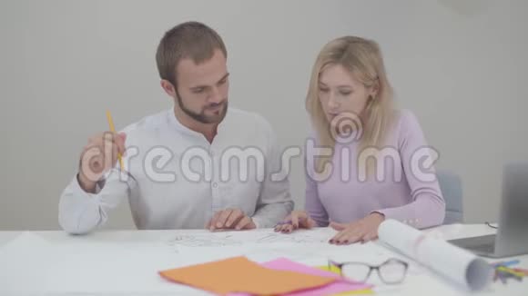 两个严肃的白种人专业人士坐在桌边检查蓝图年轻漂亮的女人和英俊的男人视频的预览图