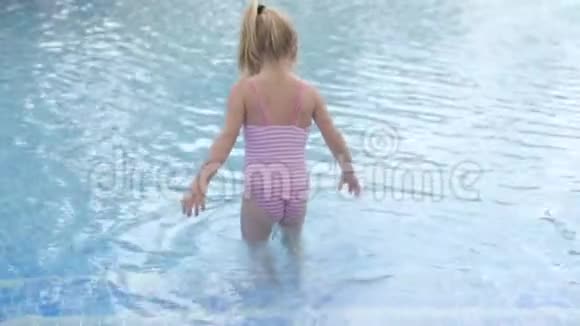一个穿着泳衣的小女孩慢慢走进一个凉爽的儿童游泳池视频的预览图
