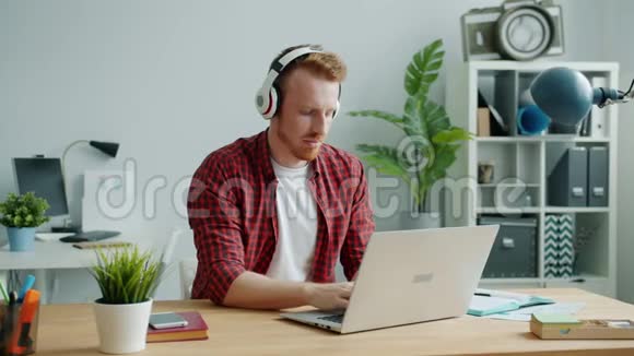 一个戴着耳机在办公室跳舞拿着笔记本电脑做生意的快乐男人视频的预览图