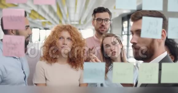 密切不同的办公室团队与男性领导头脑风暴的想法和坚持在玻璃板女办公室工作人员视频的预览图