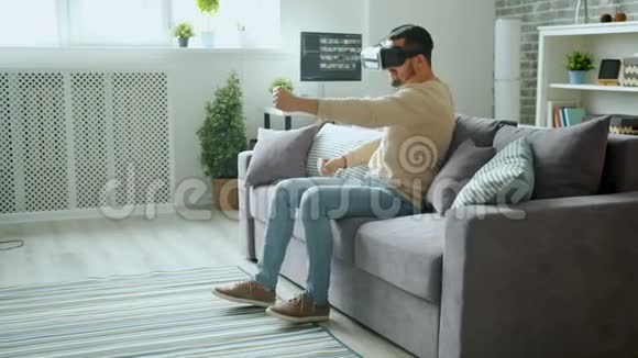 快乐的男人享受驾驶vr护目镜在家玩现代设备视频的预览图